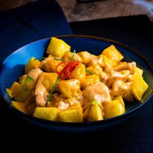 A vibrant dish of patatas bravas with rich sauce on a blue plate, perfect for culinary enthusiasts.